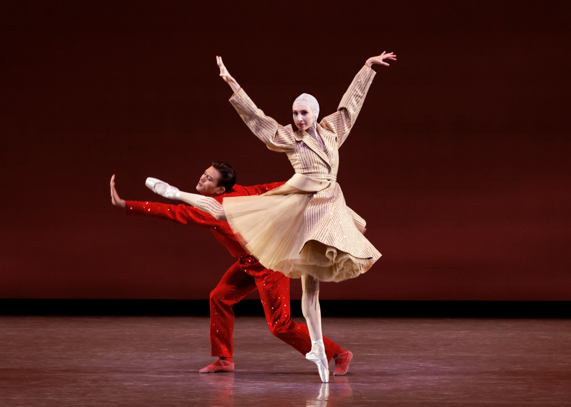 Play Time series — Play Time — partnered pose with ballerina in cream pinstriped Palomo Spain coat en pointe and cavalier in red sequined suit against deep red backdrop